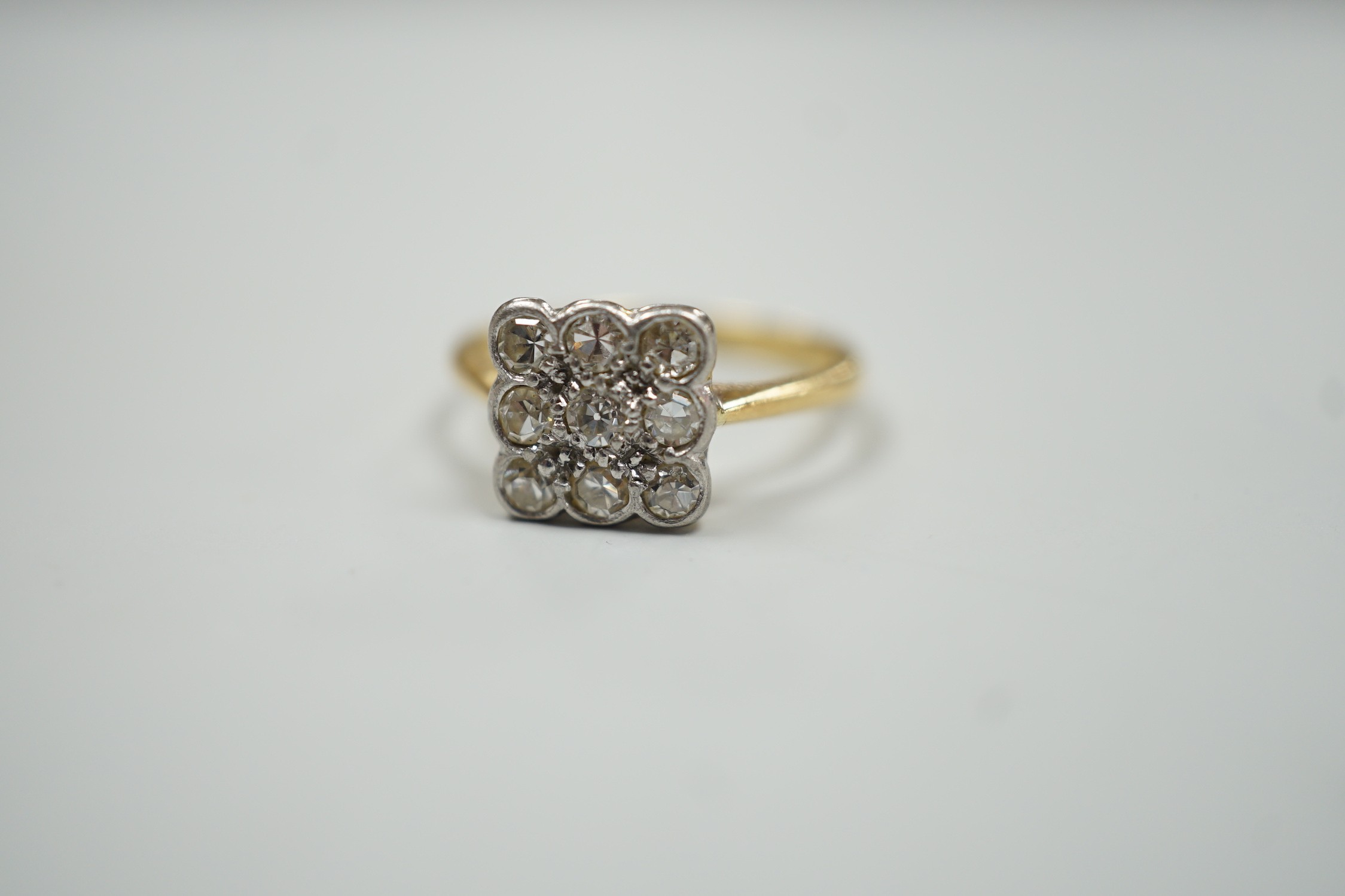An 18ct and collet set nine stone diamond cluster table ring, size K/L, gross weight 2.6 grams.
